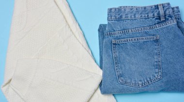 Mavi arka planda mavi kot pantolon ve beyaz örgü süveter.