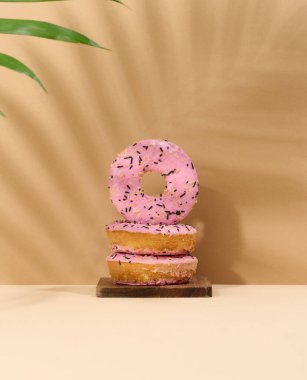 Pembe jöleli ve çok renkli serpiştirilmiş donut, palmiye yaprağından bir gölgeyle kahverengi arka plan