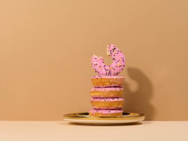 Pembe jöleli donut ve yuvarlak bir tabakta renkli şekerler serpiştirilmiş, kahverengi arka plan