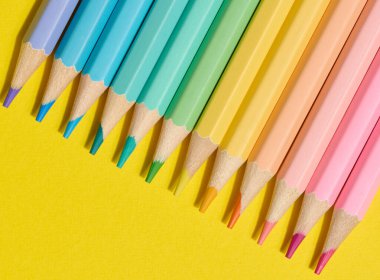 Sarı arka planda çok renkli ahşap kalemler, üst manzara.