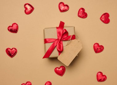 Kırmızı kurdeleli bir kutu ve bej arka planda küçük kalpler, üst görünüm