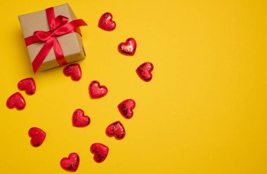 Kırmızı kurdeleli bir kutu ve sarı arka planda küçük kalpler, üst manzara.