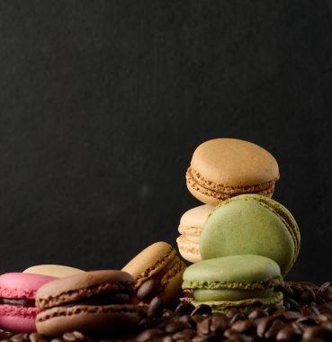 Kahve çekirdekleri ve siyah arka planda bir yığın çok renkli makaron.