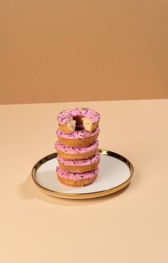 Pembe jöleli donut ve yuvarlak bir tabakta renkli şekerler serpiştirilmiş, kahverengi arka plan