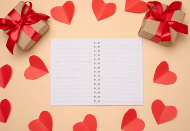 Boş beyaz çarşaflar, kırmızı kalpler ve bej arka planda hediye kutuları olan bir defter aç, üst görünüm