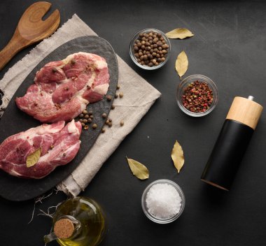 Bir tahtada iki çiğ domuz budu biftek ve pişirmek için baharat. Siyah tablonun üst görünümü