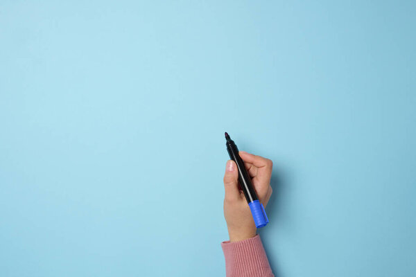 A woman's hand holds a blue felt-tip pen on a blue background, space for an inscription