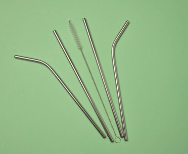 Kokteyller için metal pipetler ve yeşil arka planda temizlik fırçası.