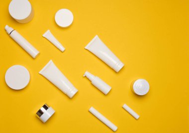 Çeşitli tipte beyaz plastik ambalajlar, şişe, kavanoz, sarı arka planda tüp. Kozmetik için konteyner, üst görünüm