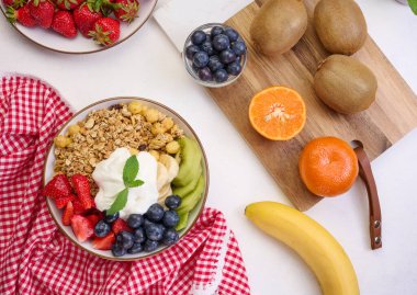 Çilekli granola, kivi, muz ve yaban mersini siyah bir masada yuvarlak bir tabakta. Sağlıklı ve lezzetli yemekler.