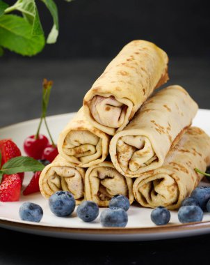 Yuvarlak tabakta doldurulmuş bir yığın kızarmış krep, siyah masa.