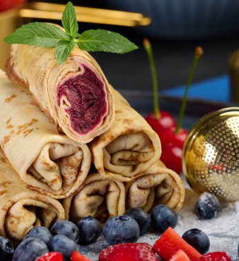 Yığınla krep yığılmış, bir tanesi kesilmiş ve böğürtlen dolgusu ile dolu. Tabak yaban mersini, çilek ve kirazla da süslenmiş.