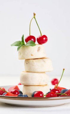 İki kiraz ve bir tutam nane ile süslenmiş dört cheesecake yığını, böğürtlen, yabanmersini, çilek ve kirazla kaplı bir tabakta. Arkaplan beyaz