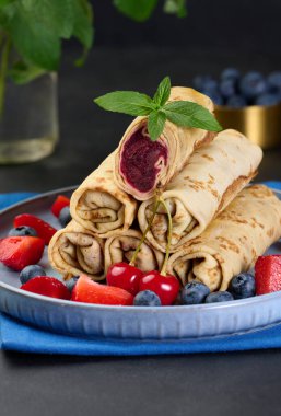 Yığınla krep yığılmış, bir tanesi kesilmiş ve böğürtlen dolgusu ile dolu. Tabak da yaban mersinli ve siyah arkaplanlı.