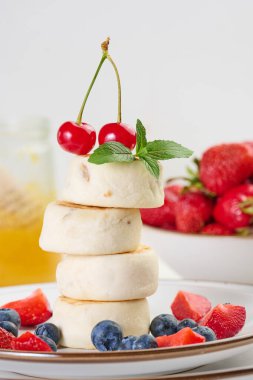 Böğürtlenli, yaban mersinli, çilekli ve kirazlı dört cheesecake yığını. Arkaplan beyaz