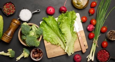 Siyah bir masada yeşil marul, brokoli, turp ve domates. Salata malzemeleri.