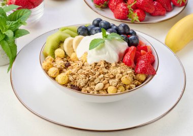 Masada yoğurt ile kaplı yuvarlak bir tabakta çilekli, kivili, muzlu ve yaban mersinli granola. Sağlıklı ve lezzetli yemekler.