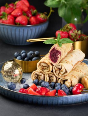 Yığınla krep yığılmış, bir tanesi kesilmiş ve böğürtlen dolgusu ile dolu. Tabak ayrıca yabanmersini, çilek ve kirazla süslenmiş.