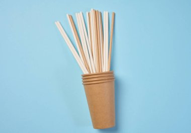 Kağıt kokteyl pipetleri ve kağıt bardaklar mavi arkaplanda, üst görünümde.