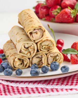 Yuvarlak bir tabakta doldurulmuş bir yığın kızarmış krep, beyaz masa.