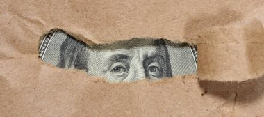 Yüz dolarlık banknotun bir parçası kağıttaki bir delikten görülebilir. Gizli ya da gizli zenginliğin sembolü, gözden uzak kalan para, ya da finansal kaynaklar.