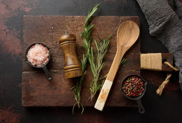 Mutfak gereçleri ve Himalaya tuzu, renkli biberler, taze biberiye ve ahşap baharat öğütücüsü de dahil olmak üzere baharatlı mutfak malzemeleri. Üst görünüm