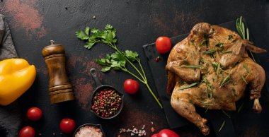 Biberiye, vişneli domates ve baharatlı bir kesme tahtasında pişmiş tavuk. Koyu arkaplan, ahşap çatal bıçak ve mutfak aletleri