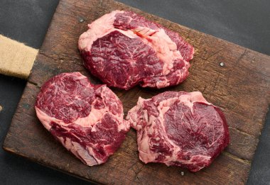 Çiğ sığır filetosu siyah bir masanın üzerindeki kesme tahtasının üzerinde duruyor.