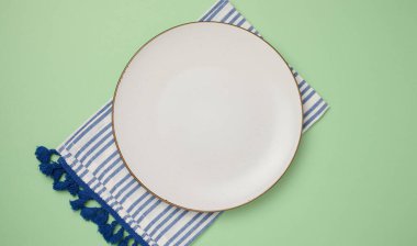 Yeşil arka planda boş seramik tabak ve mutfak havlusu, üst manzara.