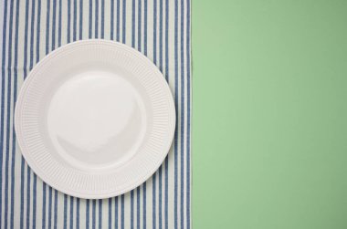 Boş seramik tabak ve yeşil arka planda mavi mutfak havlusu.