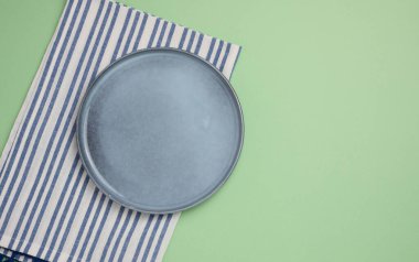 Boş seramik tabak ve yeşil arka planda mavi mutfak havlusu.