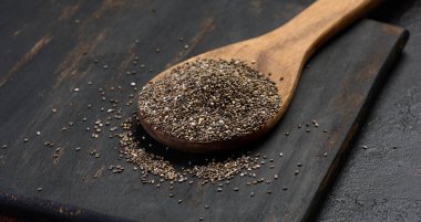 Siyah bir masada, tahta kaşıkta Chia tohumları, yakın çekim.