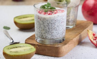 Taze meyve, nar tohumu ve kivi dilimleriyle süslenmiş iki bardak chia yoğurdu.