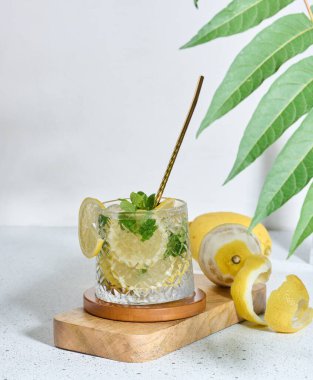 Limon dilimli şeffaf cam, nane yaprakları ve beyaz masada buz küpleri.