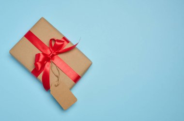 Kutu kırmızı kurdele ve kahverengi el işi kağıdıyla sarılmış. Üzerinde mavi bir arkaplan var.