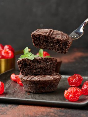 Üzerine parlak bir kiraz ve taze nane yaprağı serpiştirilmiş, koyu bir arka planda duran bir yığın çikolatalı kek.