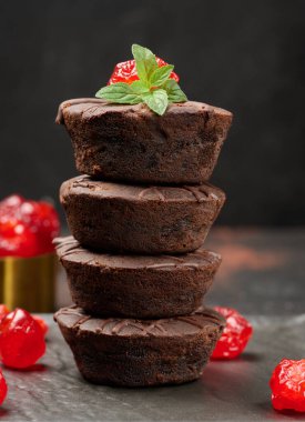 Üzerine parlak bir kiraz ve taze nane yaprağı serpiştirilmiş, koyu bir arka planda duran bir yığın çikolatalı kek..