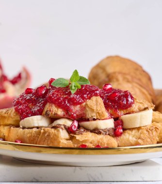 Çikolatalı kruvasan, muz parçaları ve tabakta ahududu reçeli.