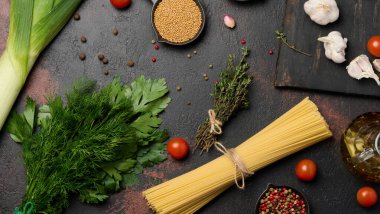Bir demet spagetti, otlar ve sarımsak koyu bir arka planda, domates ve baharatla tamamlanmış..