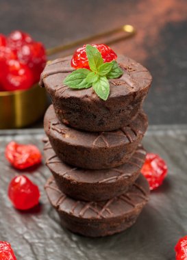 Nemli çikolatalı brownie kulesi, canlı kırmızı kiraz ve taze nane ile taçlandırılmış, çarpıcı bir sunum için koyu, karamsar bir zemin üzerine kurulmuş..