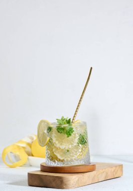 Limon dilimli şeffaf cam, nane yaprakları ve beyaz masada buz küpleri.
