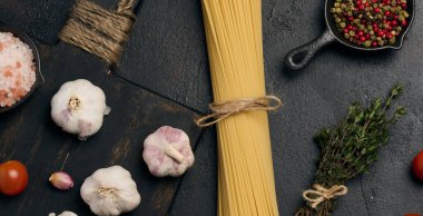 Bir demet spagetti, otlar ve sarımsak koyu bir arka planda, domates ve baharatla tamamlanmış..