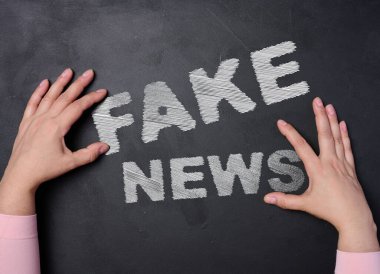 Tahtaya beyaz tebeşirle yazılmış sahte haberler ve iki kadın eli.