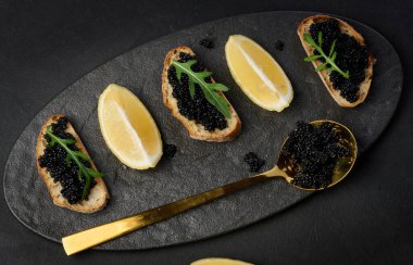 Yeşil roka yaprağı ve limon dilimleri ile süslenmiş baget ve siyah havyar sandviçi.