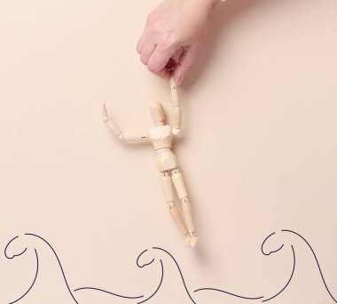 Bir ahşap manken, boyalı dalga çizgileri şeklinde tasvir edilen bir el tarafından sudan çıkarılır. Görüntü konsepti yardım, destek, kurtarma veya zor durumları aşmayı sembolize eder