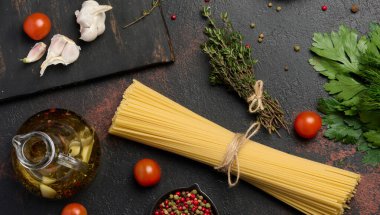 Bir demet spagetti, otlar ve sarımsak koyu bir arka planda, domates ve baharatla tamamlanmış..