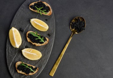 Siyah bir tabakta siyah mersin balığı havyarlı sandviçler ve limon dilimleri.
