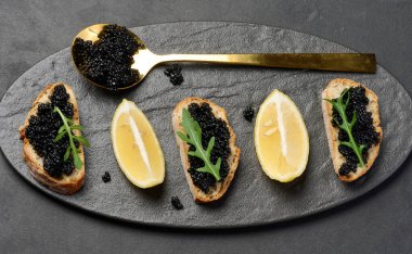 Siyah bir tabakta siyah mersin balığı havyarlı sandviçler ve limon dilimleri.