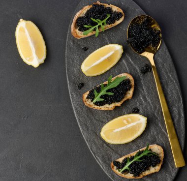 Siyah tabakta siyah mersin balıklı havyar ve limon dilimleri.