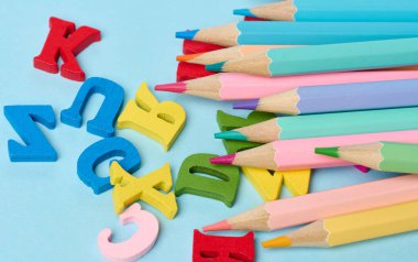 Ahşap kalemler ve mavi arka planda ahşap harfler, okul malzemeleri.